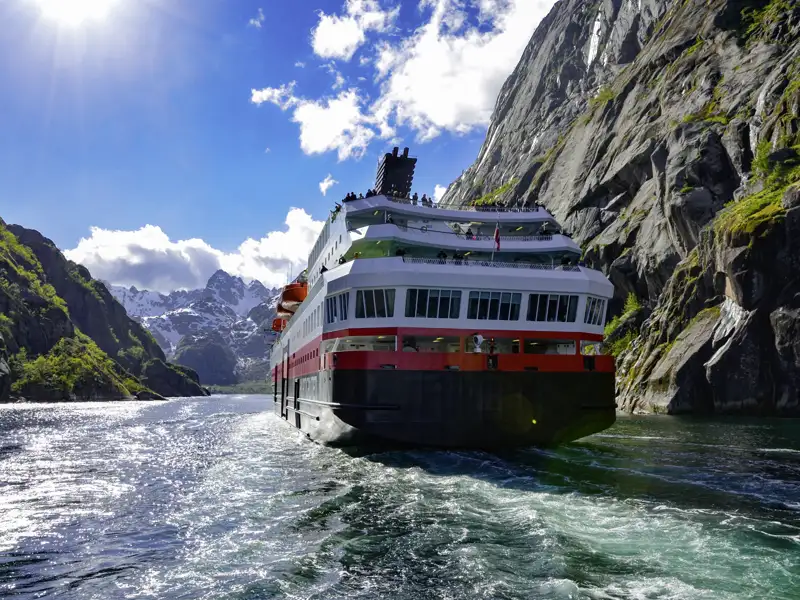 Bei der Reise gleitet Ihr Schiff durch das Wasser, vorbei an hohen Bergen.
