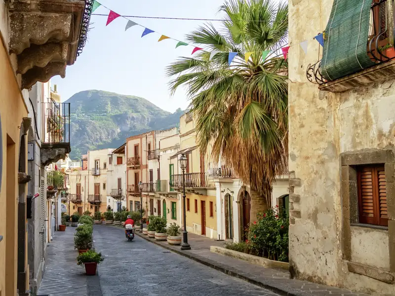 Fahnen geschmückte Straße in Lipari mit Palmen und traditioneller Architektur.