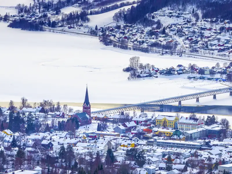 Winterliche Ansicht bei Ihrer Reise nach Lillehammer in Norwegen - mit seinen verschneiten Dächern, Kirche und einer Brücke über einen teilweise zugefrorenen Fluss.