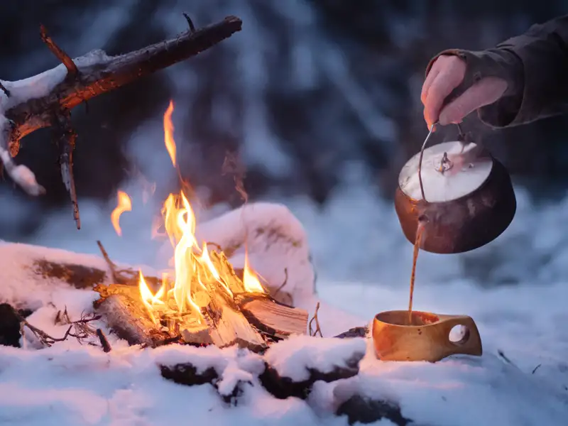 Aus einem ursprünglichen Kessel wird Kaffee in eine Holztasse neben einem romantischen Lagerfeuer gegossen. Vielleicht haben Sie auf Ihrer Reise nach Lillehammer in Norwegen auch die Gelegenheit ein solche Begegnung zu machen.