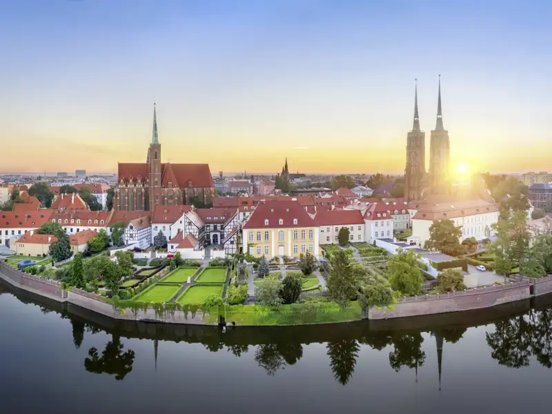 Die Dominsel in Breslau bei Sonnenaufgang, die Sie auf unserer Top-Preis-Reise besichtigen. Man sieht den Dom und historische Gebäude, die sich in der Oder spiegeln.