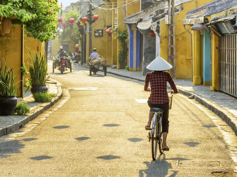 Auf Ihrer Reise sehen Sie Einheimische mit traditionellen Hüten beim Fahrradfahren durch die Altstadt von Hoi An.
