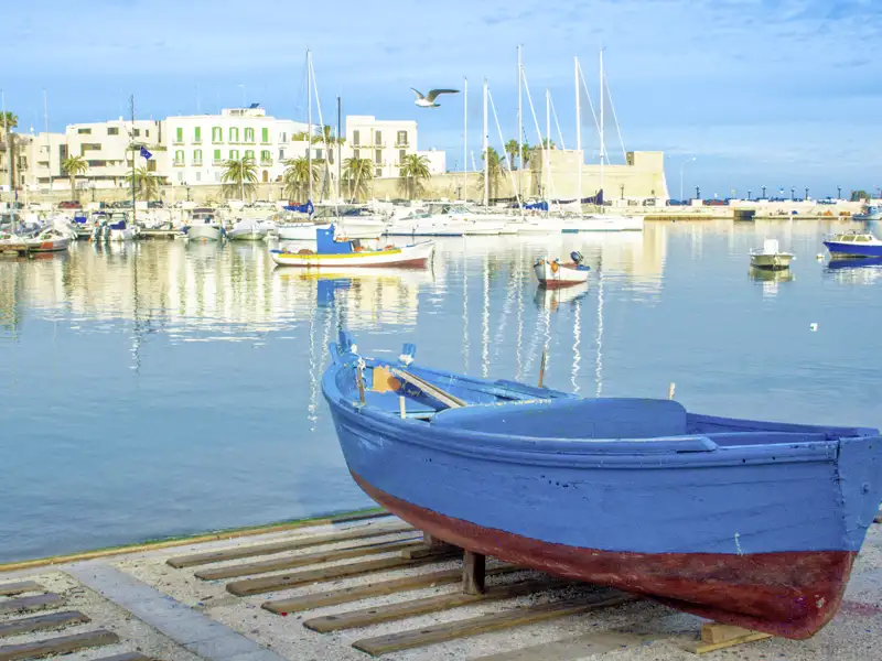 Blaues Fischerboot im Hafen von Bari, weitere Boote und Gebäude im Hintergrund.