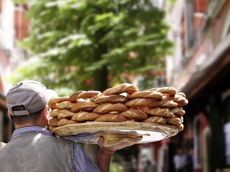 Ein Simit-Verkäufer in der Türkei trägt ein Tablett mit Sesamringen, eine kulinarische Erfahrung, die zur Entdeckung lokaler Spezialitäten gehört.
