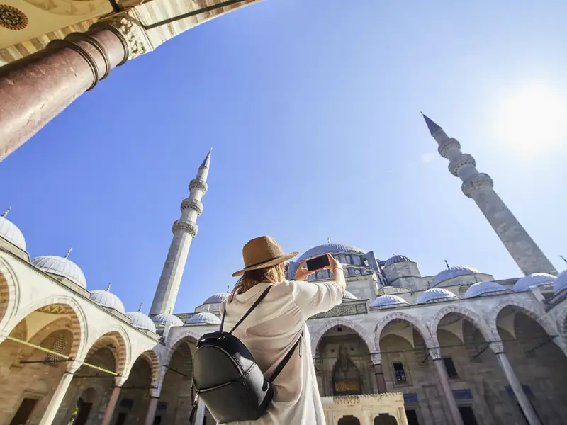 Eine Frau fotografiert während einer im Reiseverlauf inkludierten Besichtigung die beeindruckenden Kuppeln und Minarette der Blauen Moschee in Istanbul, ein Highlight dieser Top-Preis-Reise.