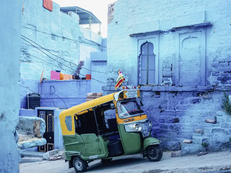 Ein buntes Tuk-Tuk steht in einer Gasse mit blau getünchten Häusern in Jodhpur, ein typischer Anblick bei der Stadterkundung in Jodhpur.