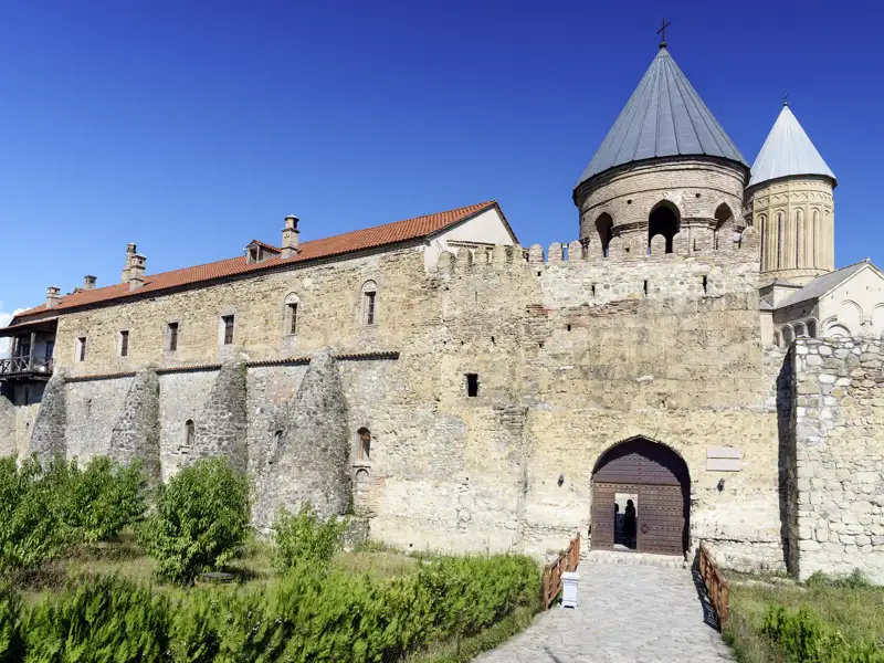 Die imposante Festungsmauer des Alaverdi-Klosters in Georgien mit der Georgskathedrale im Hintergrund bei blauem Himmel.