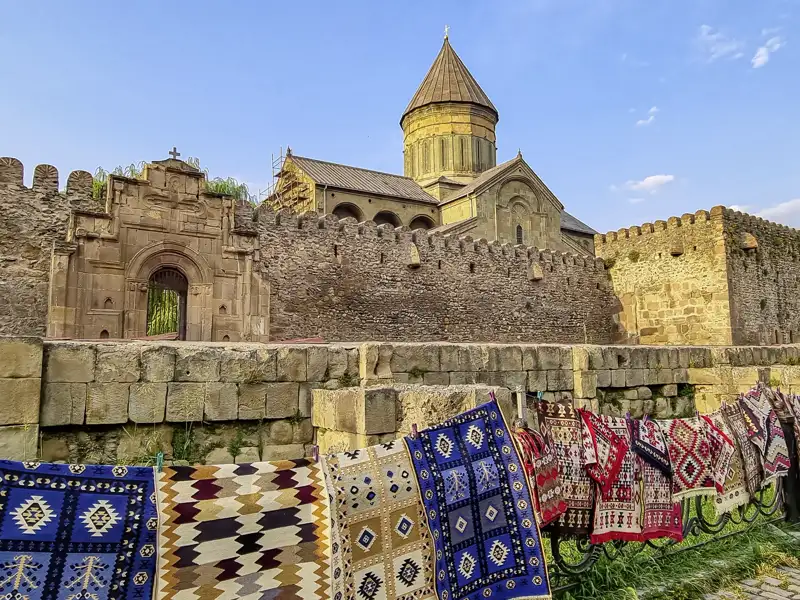 Bunte, traditionelle Teppiche hängen an einem Geländer vor der historischen Swetizchoweli-Kathedrale in Mzcheta, Georgien.