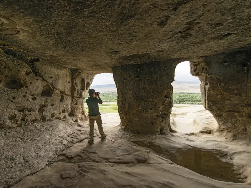 Ein Teilnehmer der Marco Polo Rundreise fotografiert die weite Landschaft aus einer Felsenhöhle in Uplisziche in Georgien.