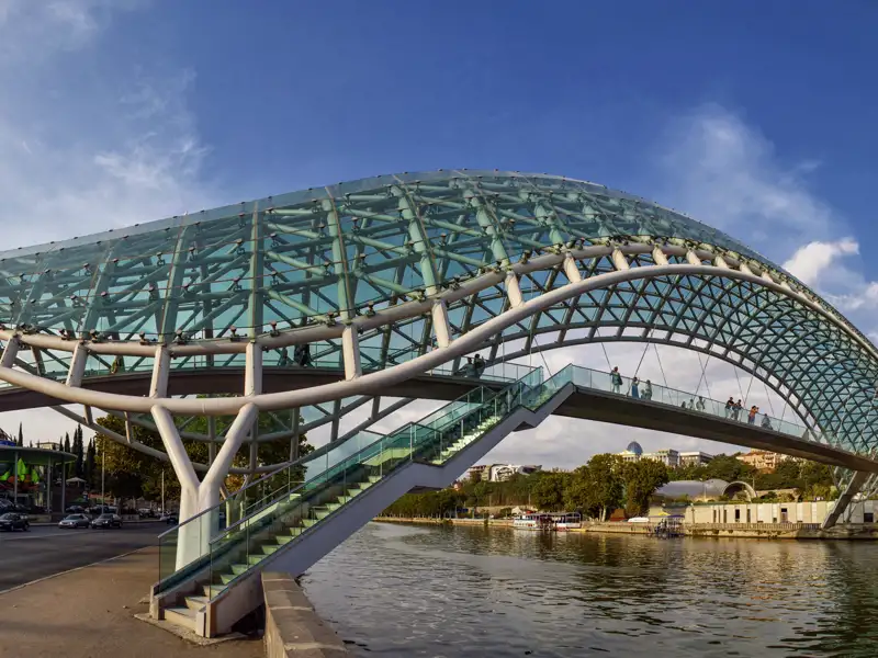 An einem sonnigen Tag überqueren Menschen die futuristische Friedensbrücke aus Glas und Stahl über den Fluss Mtkwari in Tiflis.