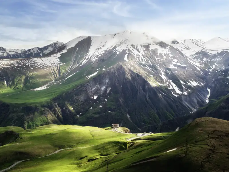 Panoramablick auf die sonnenbeschienenen grünen Hügel und die schneebedeckten Gipfel des Kaukasus in Georgien bei Gudauri.