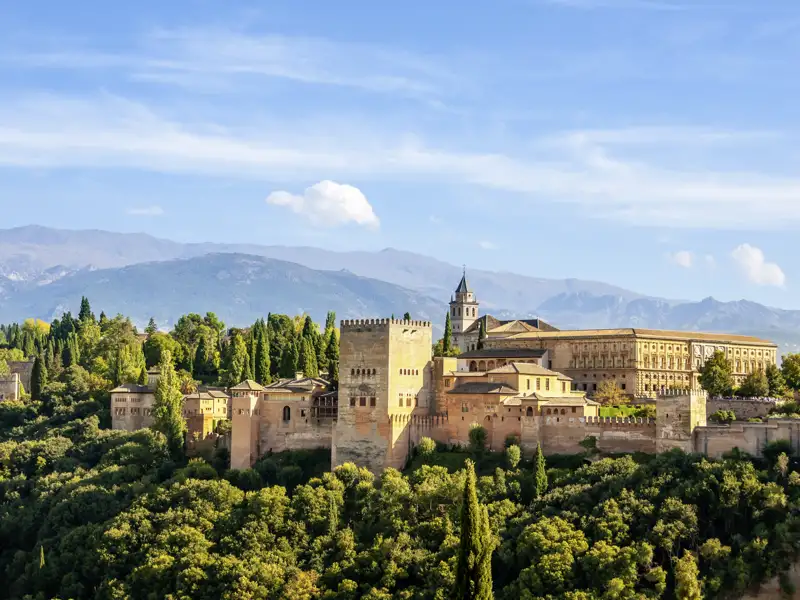 Auf unserer Rundreise durch Andalusien haben wir einen Panoramablick auf die Alhambra mit ihren Türmen, Mauern und Gebäuden, eingebettet in die Landschaft der Sierra Nevada.