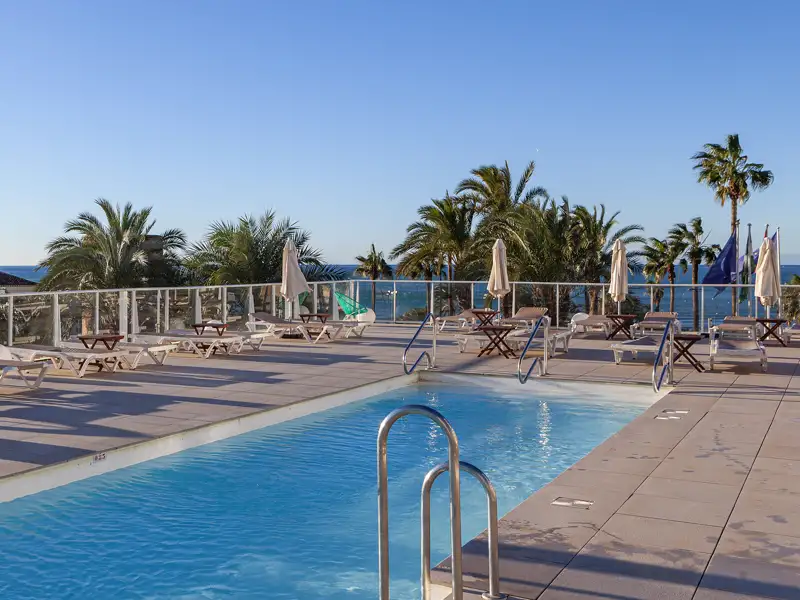 Eine Möglichkeit für einen freien Tag während der Rundreise durch Andalusien: Die Sonnenterrasse des Hotels mit Swimmingpool, Liegestühlen und Palmen, die vorbei an Palmen einen Blick auf das Meer bietet.