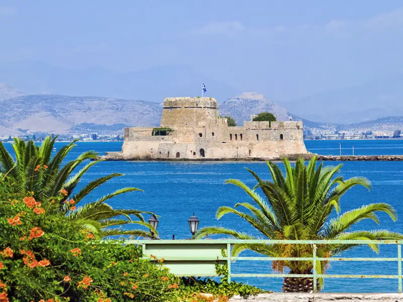 Blick von der Promenade mit Palmen auf die historische Bourtzi-Festung im blauen Meer vor der Hafenstadt Nafplio in Griechenland.