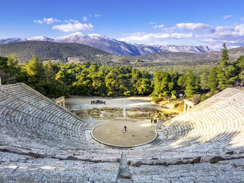 Eine kleine Reisegruppe erkundet das antike Freilichttheater von Epidauros vor einer beeindruckenden Kulisse aus Pinien und Bergen.