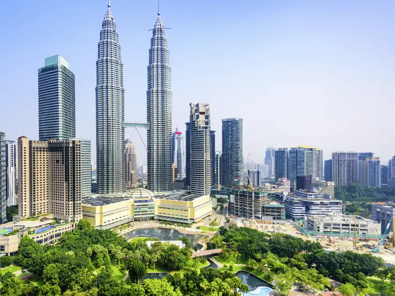Auf Ihrer Reise sehen Sie die ikonischen Petronas Twin Towers. Sie ragen über die Skyline von Kuala Lumpur, der weitläufige KLCC Park liegt im Vordergrund.