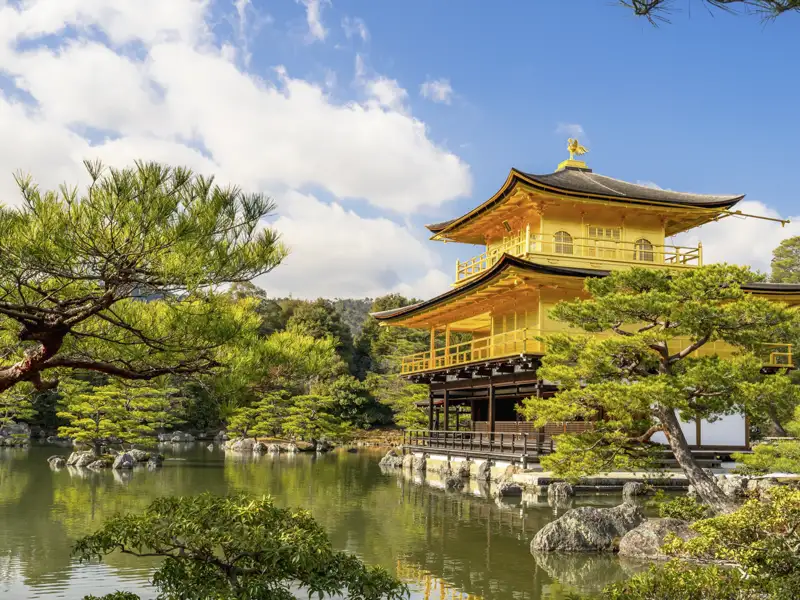 Der goldene Kinkaku-ji Pavillon in Kyoto spiegelt sich an einem sonnigen Tag malerisch im umgebenden Teich.