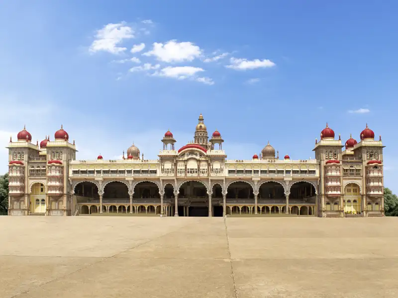 Außenansicht des Mysore-Palasts mit seinen vielen Kuppeln und Bögen vor blauem Himmel.
