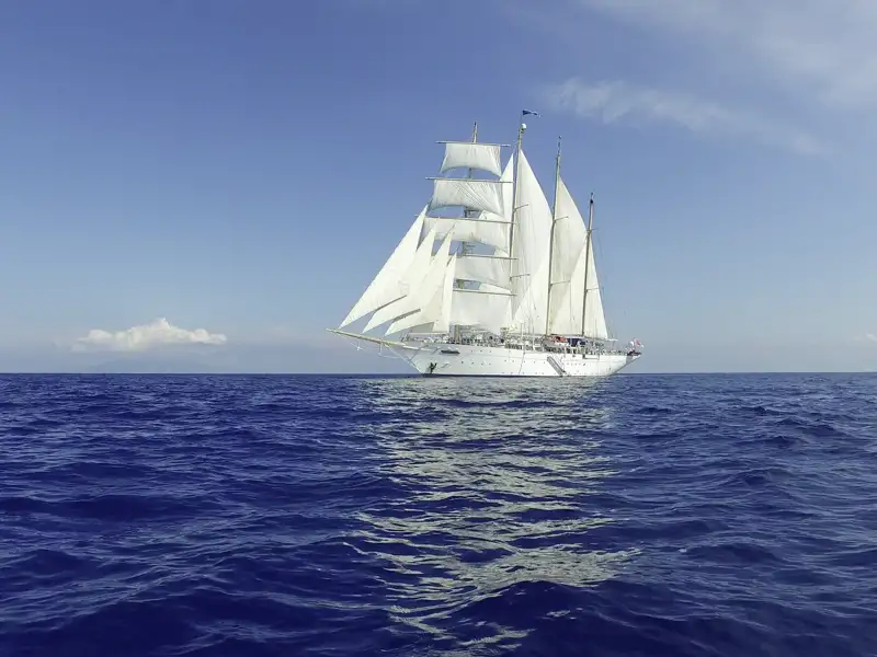 Der majestätische Großsegler Star Flyer mit weißen Segeln kreuzt auf dem blauen Meer entlang der Küste der Kleinen Antillen.
