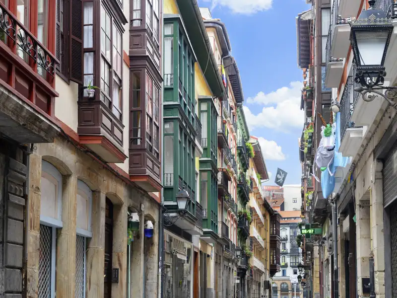 Traditionelle Gasse in der Altstadt Casco Viejo von Bilbao mit hohen Häusern, bunten Fassaden und typischen, verglasten Erkerbalkonen.