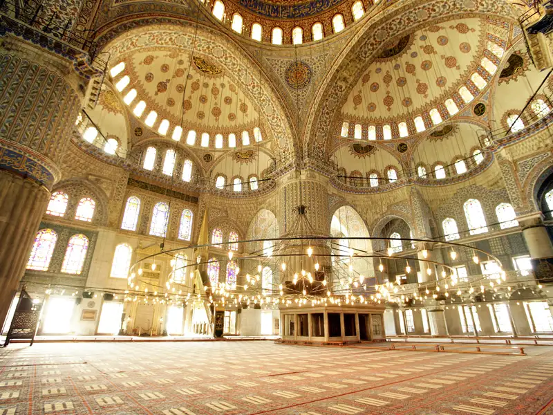 Weitläufiger Innenraum der Blauen Moschee in Istanbul mit ornamental verziertem Gewölbe und riesigem, tief hängendem Leuchter.