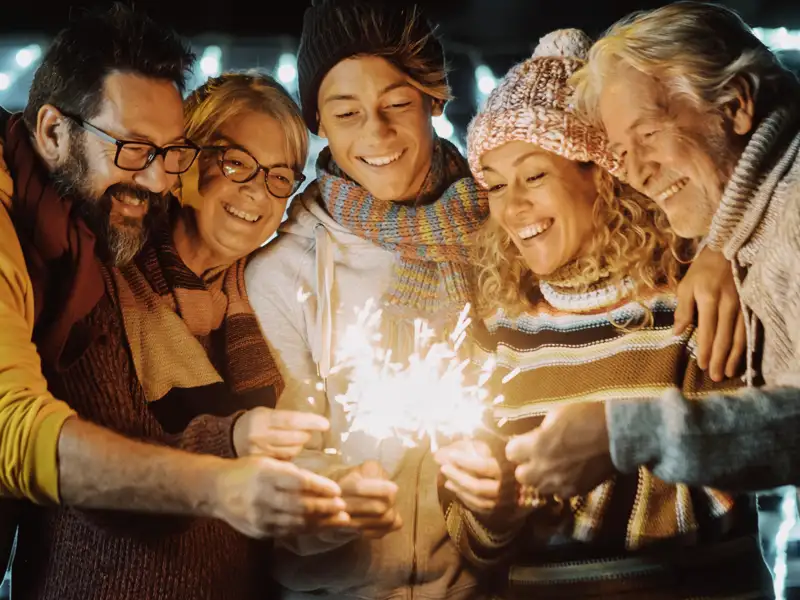 Eine bunt gemischte Reisegruppe begrüßt lachend das neue Jahr und hält gemeinsam leuchtende Wunderkerzen in der Nacht.