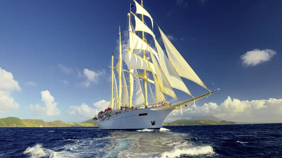 Der majestätische Großsegler Star Flyer mit weißen Segeln kreuzt auf dem blauen Meer entlang der Küste der Kleinen Antillen.