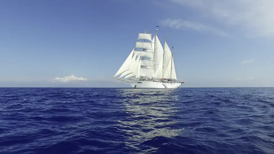 Der majestätische Großsegler Star Flyer mit weißen Segeln kreuzt auf dem blauen Meer entlang der Küste der Kleinen Antillen.