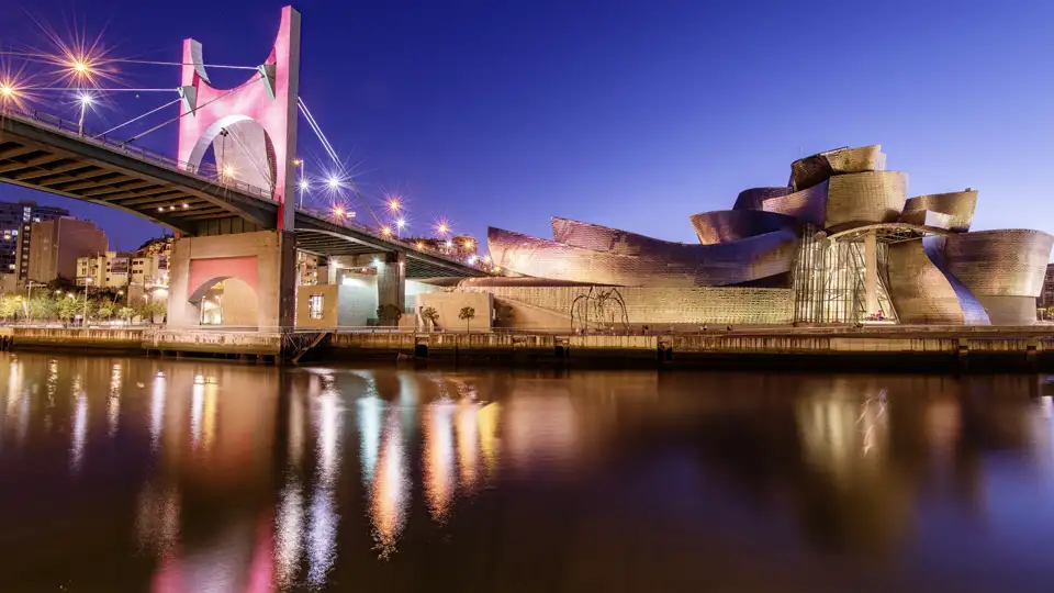 Brücke Puente La Salve und Guggenheim-Museum in Bilbao hell beleuchtet unter dem Nachthimmel.