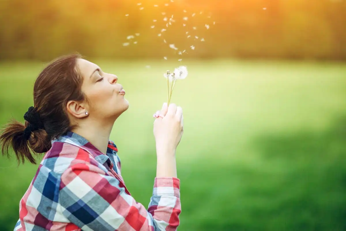 Sommerliche Szene mit einer Frau, die Löwenzahnblüten bläst.