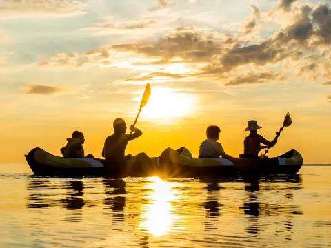 Eine Gruppe von Menschen paddelt auf dem Wasser, während Sonnenuntergang.